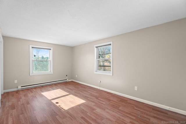 empty room with a wealth of natural light, a baseboard radiator, a textured ceiling, and light hardwood / wood-style flooring