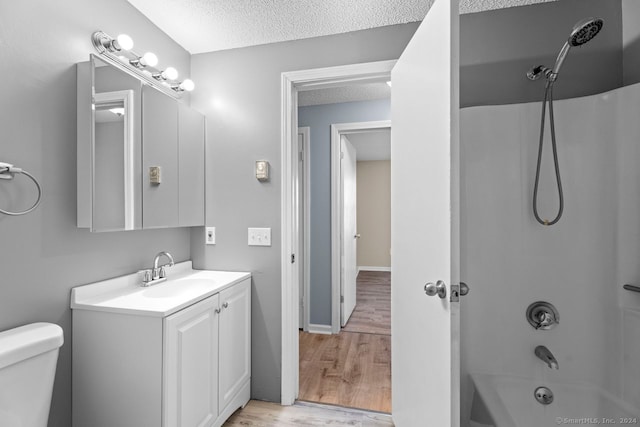 full bathroom with toilet, a textured ceiling, hardwood / wood-style flooring, shower / bathing tub combination, and vanity