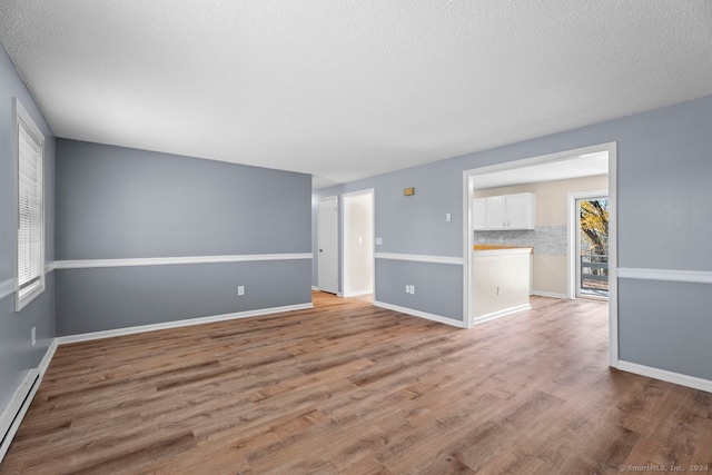 empty room with a baseboard heating unit, light hardwood / wood-style floors, and a textured ceiling