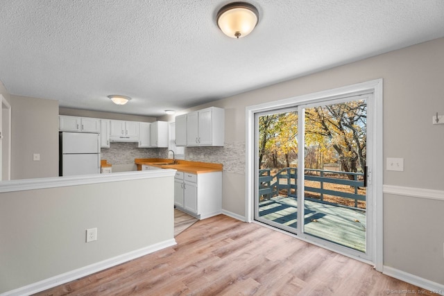 kitchen with wooden counters, white cabinetry, decorative backsplash, and white fridge