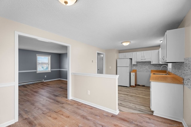 kitchen with light hardwood / wood-style floors, white refrigerator, white cabinets, baseboard heating, and backsplash