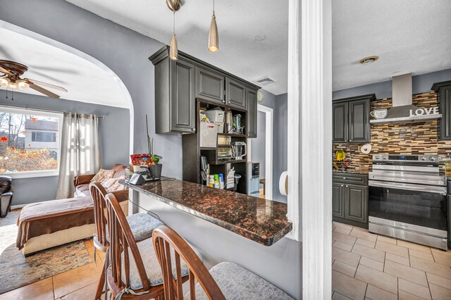 kitchen featuring ceiling fan, backsplash, stainless steel electric range, gray cabinets, and wall chimney range hood