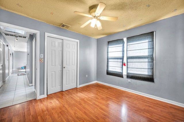 unfurnished bedroom with light hardwood / wood-style floors, a textured ceiling, ceiling fan, and a closet