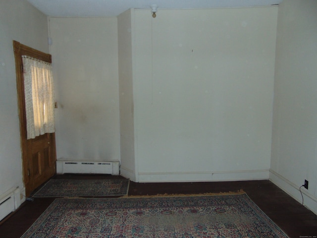 unfurnished room featuring dark wood-type flooring and baseboard heating