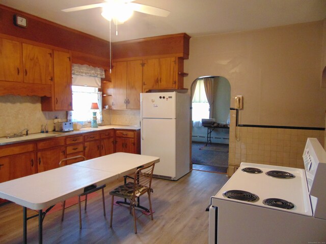 kitchen featuring sink, baseboard heating, ceiling fan, light hardwood / wood-style flooring, and white appliances