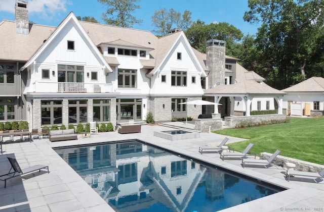 rear view of property with a balcony, a yard, a patio, and a pool with hot tub