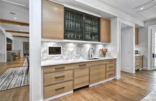 bar with hardwood / wood-style flooring, beamed ceiling, backsplash, sink, and light stone counters