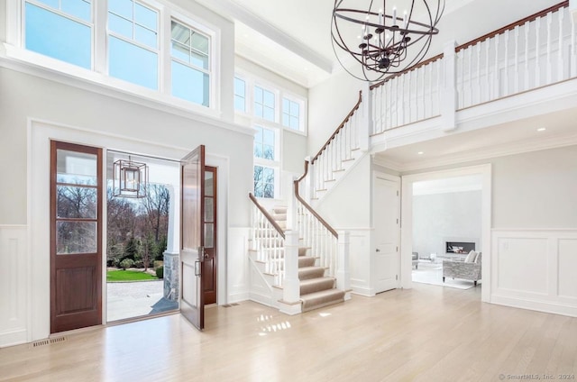 foyer entrance featuring light hardwood / wood-style floors, a towering ceiling, ornamental molding, and a chandelier