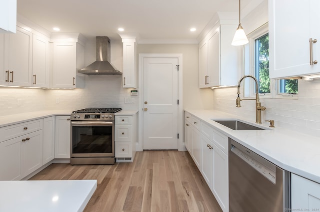 kitchen with appliances with stainless steel finishes, wall chimney exhaust hood, sink, white cabinets, and hanging light fixtures