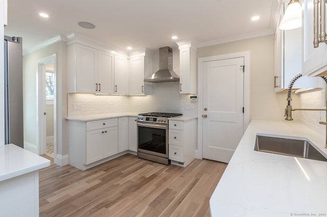 kitchen featuring white cabinets, sink, wall chimney exhaust hood, light wood-type flooring, and gas stove