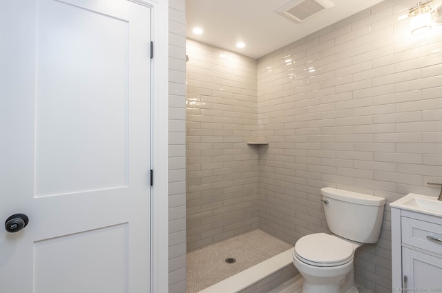 bathroom featuring a tile shower, vanity, toilet, and tile walls