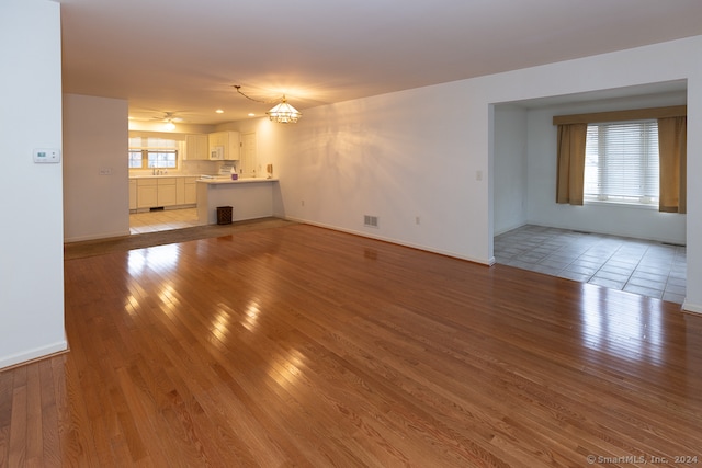 unfurnished living room with ceiling fan with notable chandelier, light hardwood / wood-style floors, a healthy amount of sunlight, and sink