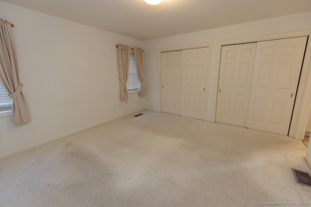 unfurnished bedroom with light carpet and multiple closets