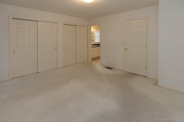 unfurnished bedroom featuring light colored carpet, multiple closets, and ensuite bath