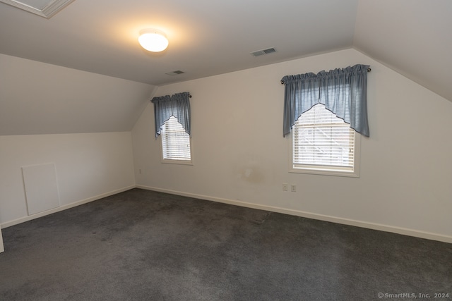 additional living space with dark colored carpet and vaulted ceiling