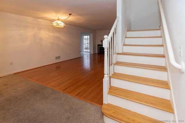 staircase with hardwood / wood-style flooring and a notable chandelier