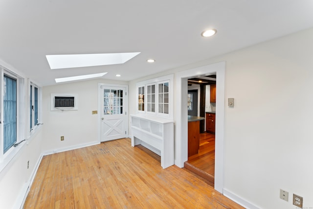 unfurnished room with lofted ceiling with skylight, light wood-type flooring, and a wall mounted air conditioner