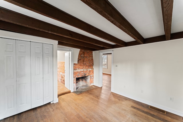 unfurnished living room with brick wall, beamed ceiling, light hardwood / wood-style floors, and a brick fireplace