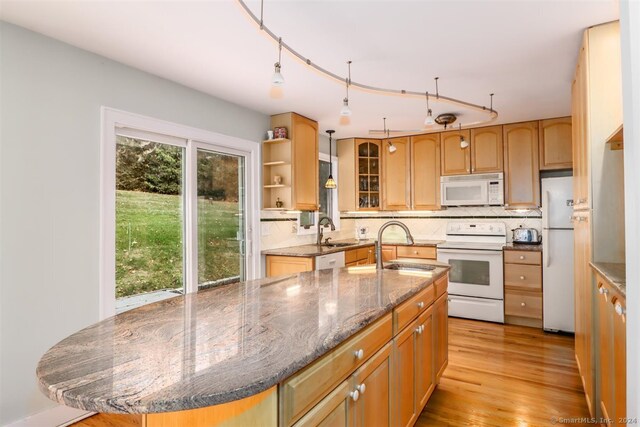 kitchen featuring white appliances, tasteful backsplash, an island with sink, dark stone countertops, and light hardwood / wood-style flooring