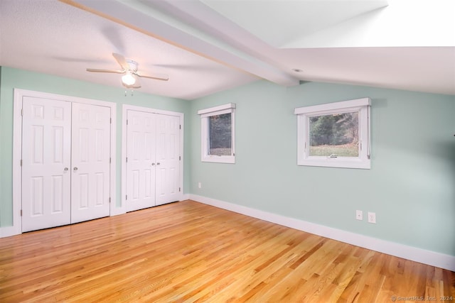 unfurnished bedroom featuring hardwood / wood-style floors, multiple closets, lofted ceiling with beams, and ceiling fan