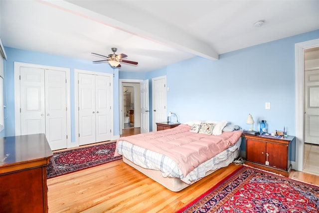 bedroom with ceiling fan, hardwood / wood-style flooring, beam ceiling, and two closets