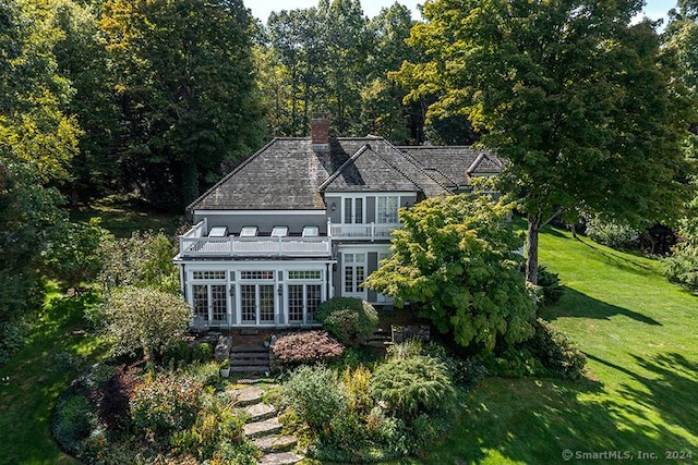 view of front facade with french doors, a chimney, a front yard, and a balcony