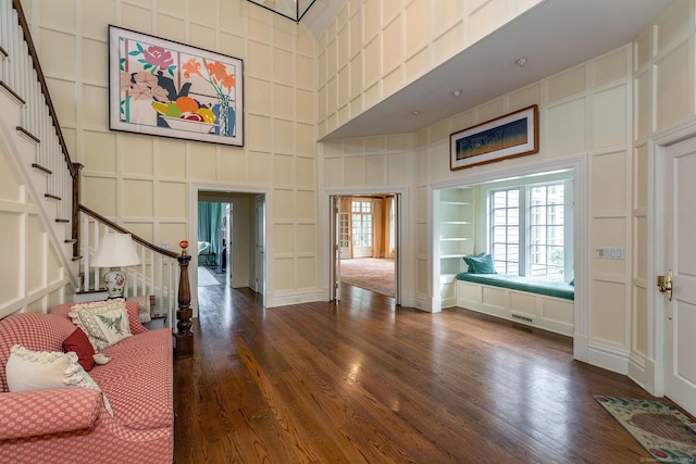 foyer entrance with a towering ceiling, stairs, a decorative wall, and wood finished floors