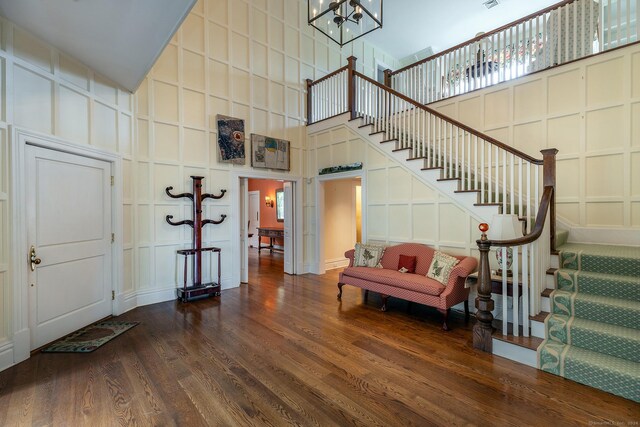 entrance foyer with a notable chandelier, a decorative wall, stairway, a towering ceiling, and dark wood-type flooring