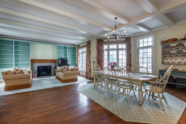 dining area with a chandelier, a glass covered fireplace, beamed ceiling, and wood finished floors