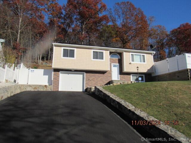 bi-level home with brick siding, a front lawn, fence, aphalt driveway, and an attached garage