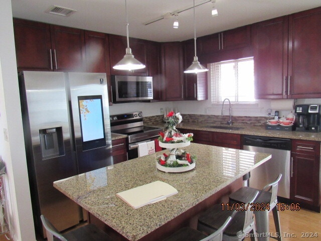 kitchen featuring hanging light fixtures, light stone counters, stainless steel appliances, sink, and a center island