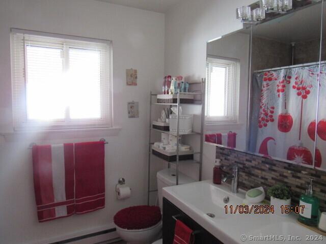 bathroom with a baseboard heating unit, curtained shower, toilet, and vanity