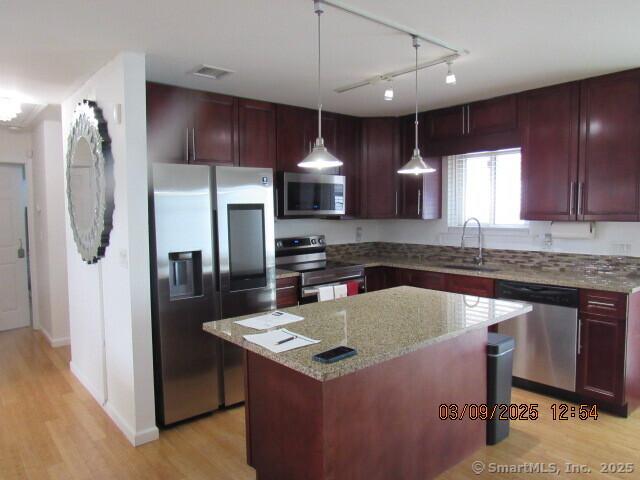 kitchen featuring light wood finished floors, visible vents, dark brown cabinets, stainless steel appliances, and a sink