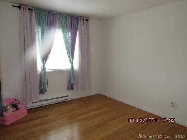 spare room with baseboards, baseboard heating, and wood finished floors