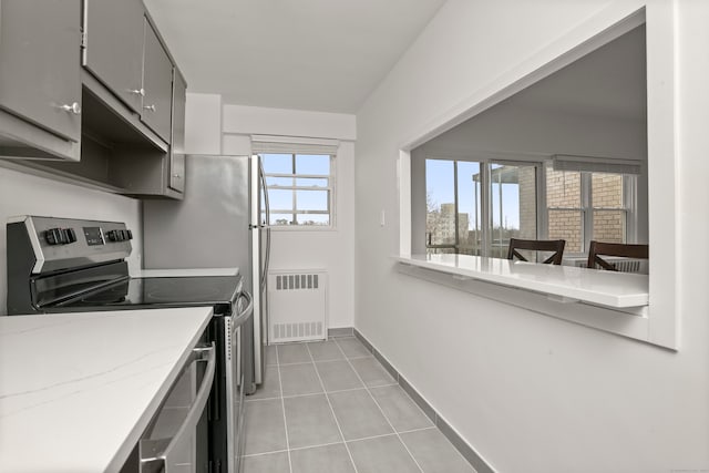 kitchen with stainless steel range with electric stovetop, light tile patterned floors, radiator, and a wealth of natural light