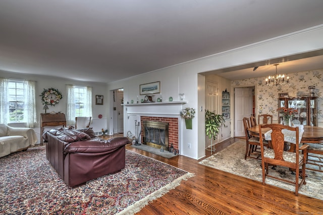 living room with crown molding, dark hardwood / wood-style flooring, a chandelier, and a brick fireplace