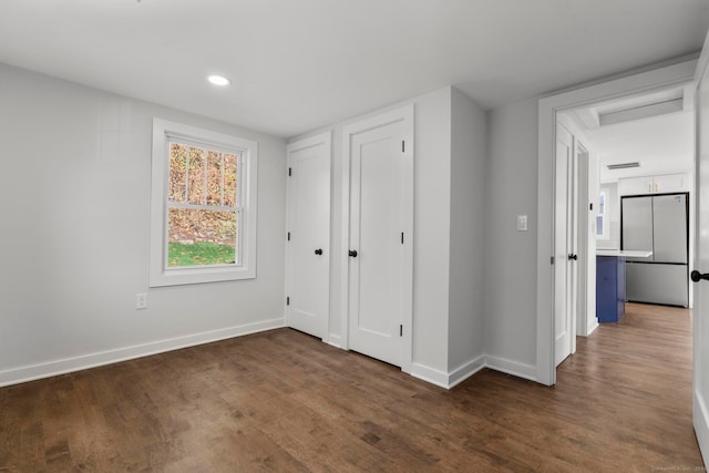 unfurnished bedroom with stainless steel fridge and dark hardwood / wood-style flooring