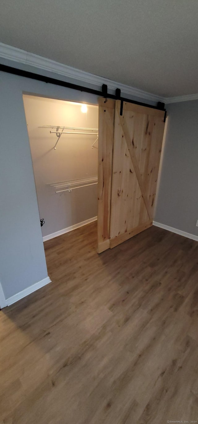 interior space featuring wood-type flooring, a barn door, and ornamental molding