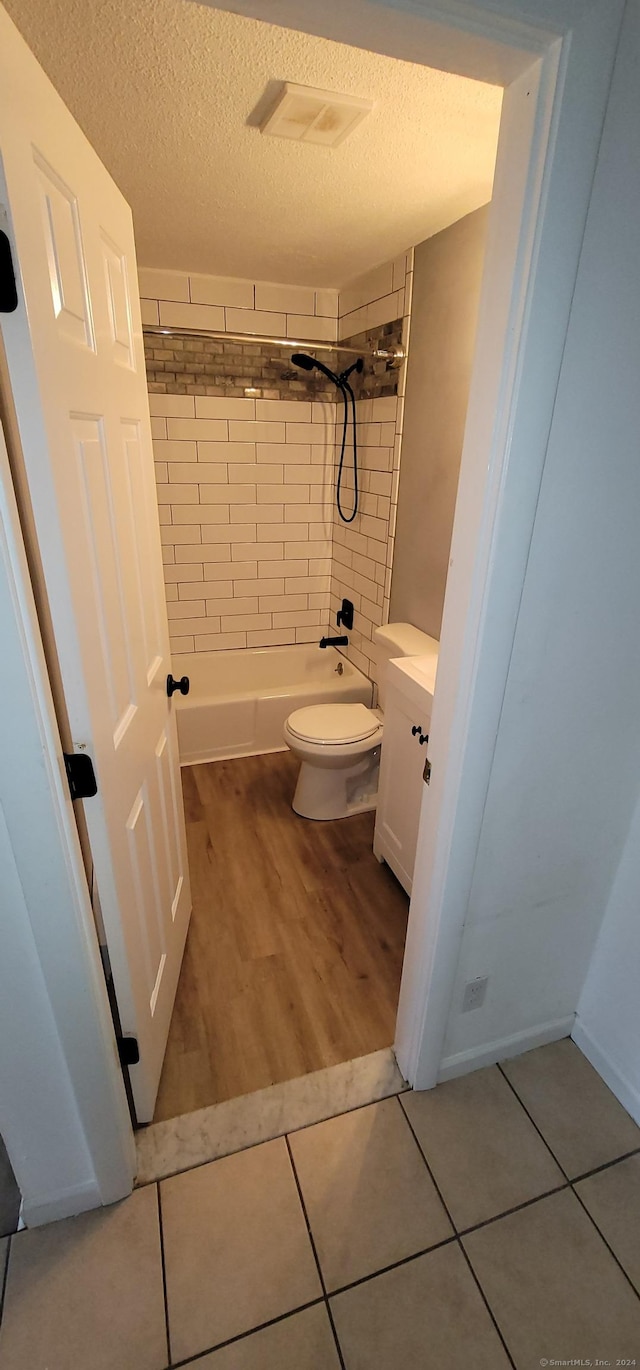 full bathroom with a textured ceiling, hardwood / wood-style flooring, toilet, and tiled shower / bath combo