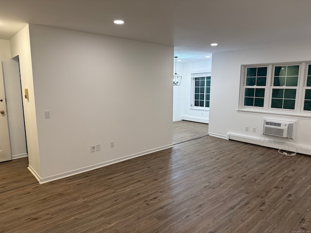 empty room with baseboard heating, a wall unit AC, dark hardwood / wood-style floors, and a chandelier