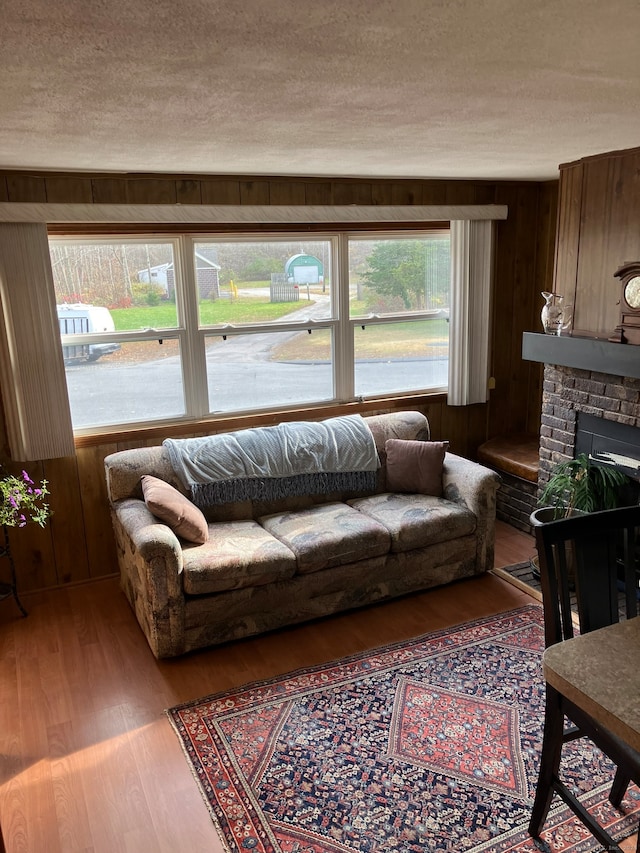 living room featuring a textured ceiling, a fireplace, wood-type flooring, and wooden walls