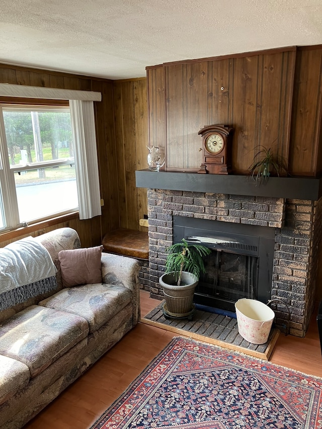 living room with a brick fireplace, light wood-type flooring, a textured ceiling, and wooden walls