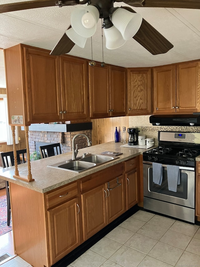 kitchen with kitchen peninsula, sink, light tile patterned floors, and gas range