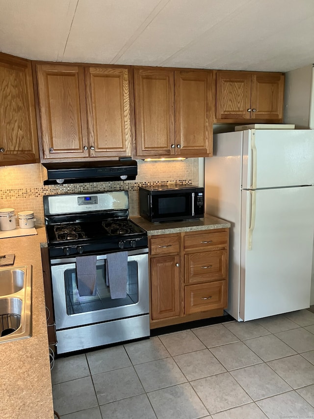 kitchen with ventilation hood, light tile patterned floors, white refrigerator, and gas stove