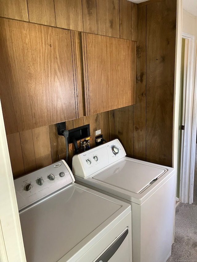 clothes washing area with washing machine and clothes dryer, cabinets, wood walls, and carpet