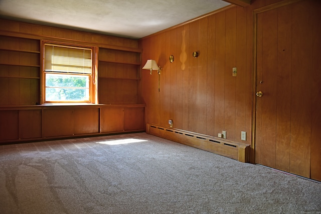 spare room with wooden walls, carpet flooring, a baseboard radiator, and built in shelves