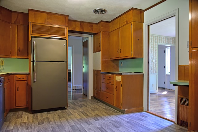 kitchen with crown molding, a textured ceiling, light wood-type flooring, and stainless steel refrigerator