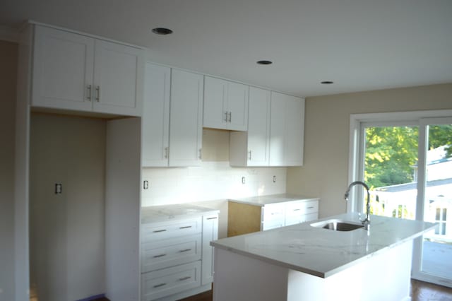 kitchen featuring an island with sink, white cabinetry, sink, and light stone counters