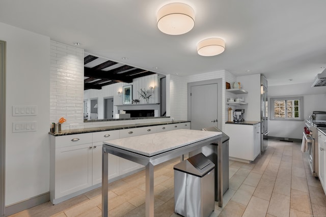 kitchen with white cabinetry, high quality appliances, open shelves, dark stone counters, and beamed ceiling