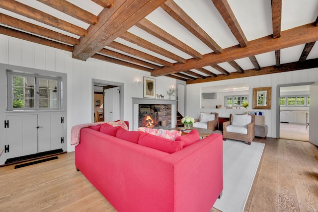 living area featuring light wood-style floors, beam ceiling, a brick fireplace, and healthy amount of natural light